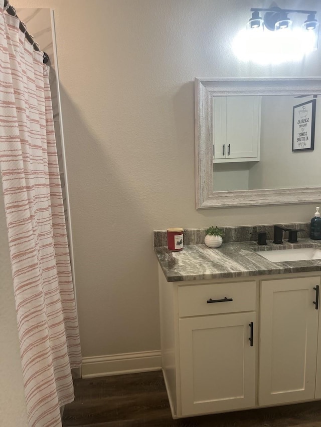 bathroom with curtained shower, vanity, baseboards, and wood finished floors