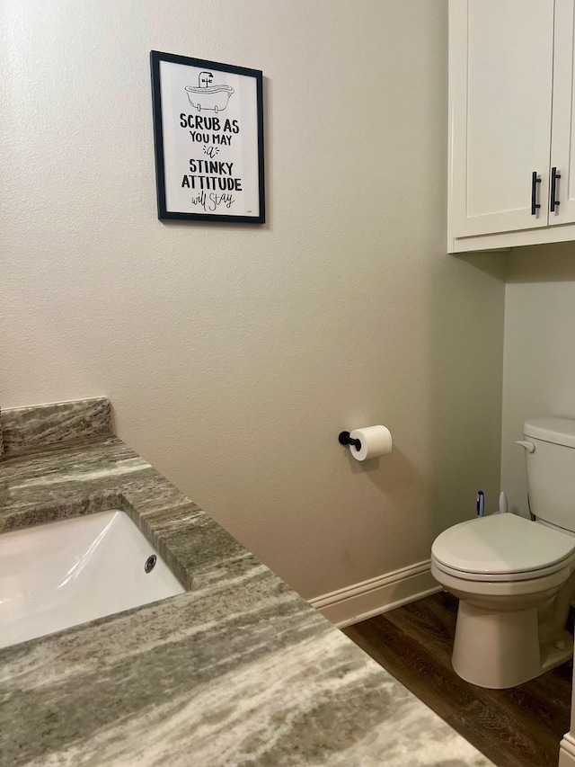 half bath featuring wood finished floors, toilet, and baseboards