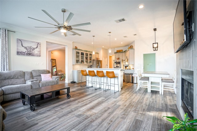 living area with visible vents, a ceiling fan, ornamental molding, wood finished floors, and recessed lighting