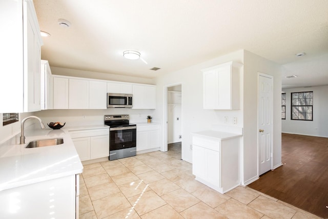 kitchen featuring white cabinetry, appliances with stainless steel finishes, light countertops, and a sink