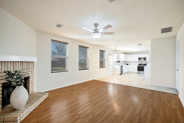 unfurnished living room with a brick fireplace, visible vents, and light wood-style floors