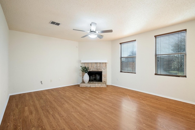 unfurnished living room featuring a fireplace, wood finished floors, visible vents, and a ceiling fan