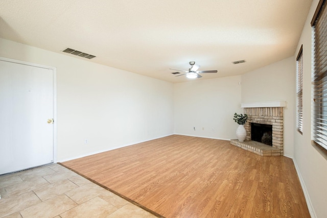 unfurnished living room with light wood-type flooring, visible vents, a fireplace, and ceiling fan