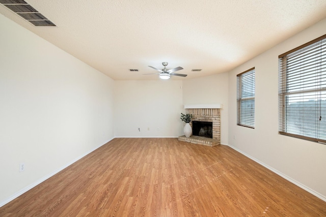 unfurnished living room featuring light wood-type flooring, a brick fireplace, ceiling fan, and visible vents