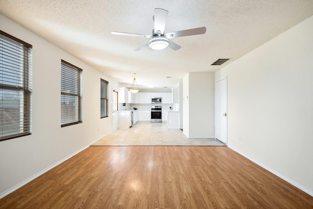 interior space featuring a textured ceiling, ceiling fan, visible vents, baseboards, and light wood-type flooring