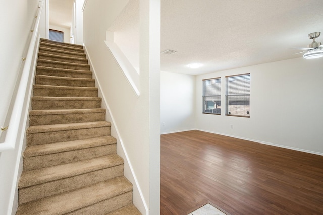 stairs featuring visible vents, a ceiling fan, a textured ceiling, wood finished floors, and baseboards