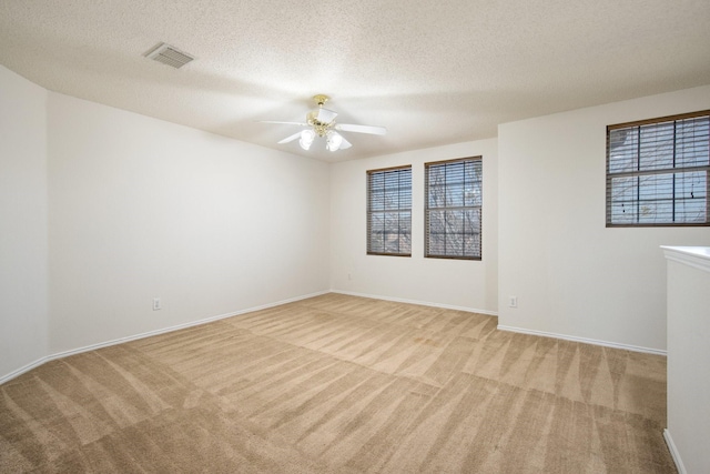 unfurnished room featuring light colored carpet, visible vents, a ceiling fan, a textured ceiling, and baseboards