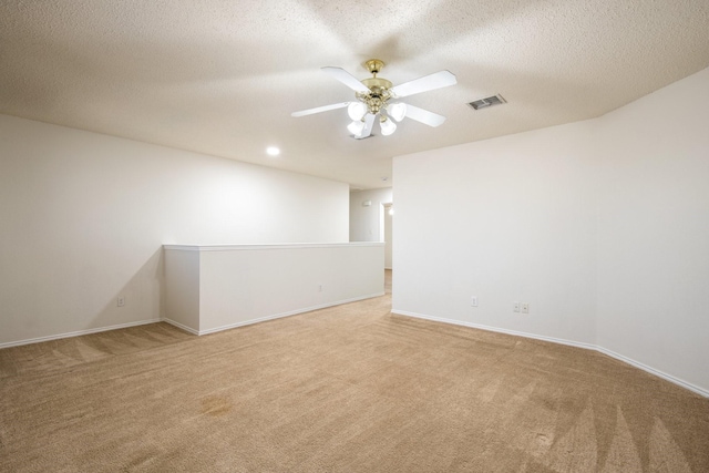 spare room with light carpet, a textured ceiling, visible vents, and a ceiling fan