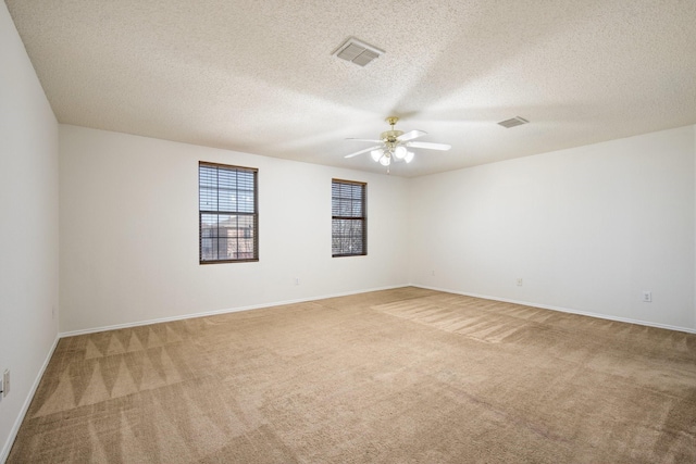 carpeted empty room featuring a ceiling fan, visible vents, a textured ceiling, and baseboards