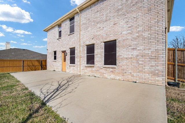 rear view of house featuring brick siding, fence, and a patio