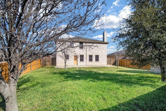 back of property with a fenced backyard, a yard, and a chimney