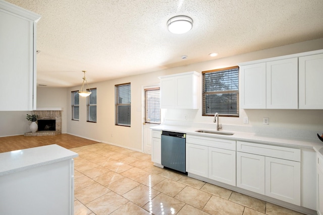 kitchen featuring dishwashing machine, light countertops, a fireplace, white cabinetry, and a sink