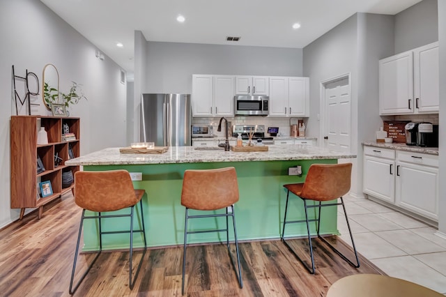 kitchen featuring appliances with stainless steel finishes, white cabinetry, backsplash, and a kitchen breakfast bar