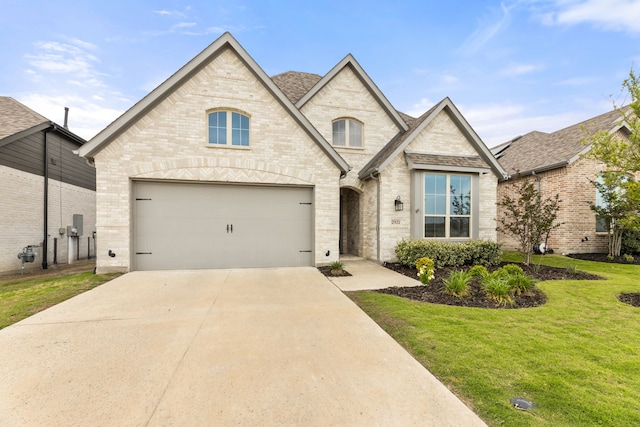 french country inspired facade with a front yard, concrete driveway, and brick siding