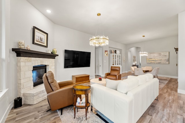 living area featuring baseboards, arched walkways, wood finished floors, an inviting chandelier, and a fireplace