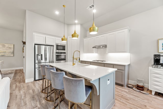 kitchen with stainless steel appliances, exhaust hood, a sink, visible vents, and decorative backsplash