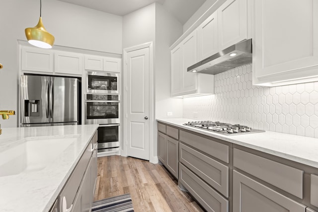 kitchen featuring light wood finished floors, decorative backsplash, stainless steel appliances, gray cabinetry, and under cabinet range hood