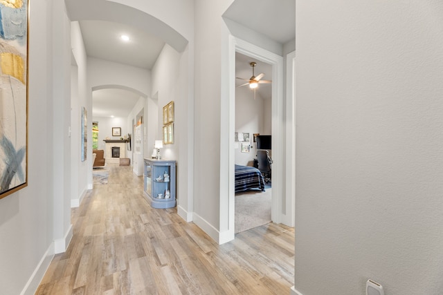 corridor with arched walkways, baseboards, and light wood finished floors