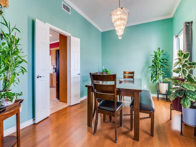 dining room with a notable chandelier, visible vents, crown molding, and wood finished floors