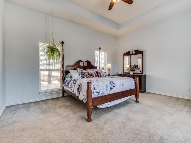 bedroom with baseboards, ceiling fan, a tray ceiling, and light colored carpet