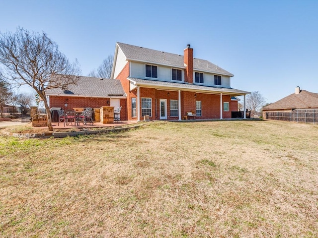 rear view of property with brick siding, fence, a yard, a chimney, and a patio area