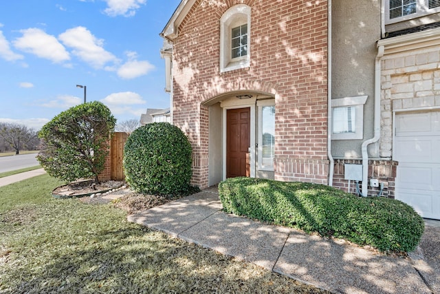 entrance to property with a garage, brick siding, and stucco siding