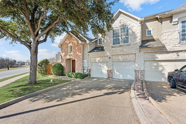 townhome / multi-family property with aphalt driveway, stone siding, brick siding, and an attached garage