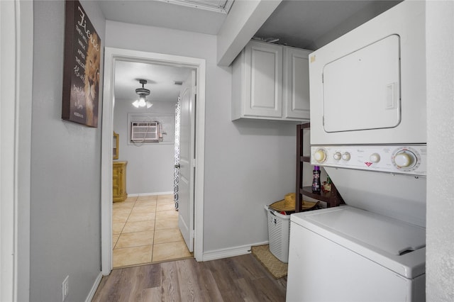 laundry room with stacked washer / dryer, baseboards, a wall mounted AC, light wood-type flooring, and cabinet space