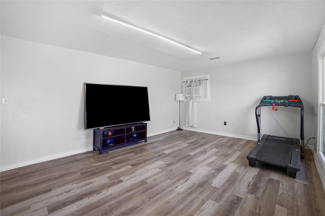 exercise room featuring visible vents, a textured ceiling, baseboards, and wood finished floors