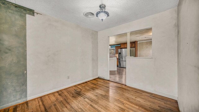 unfurnished room with a textured ceiling, baseboards, and wood-type flooring