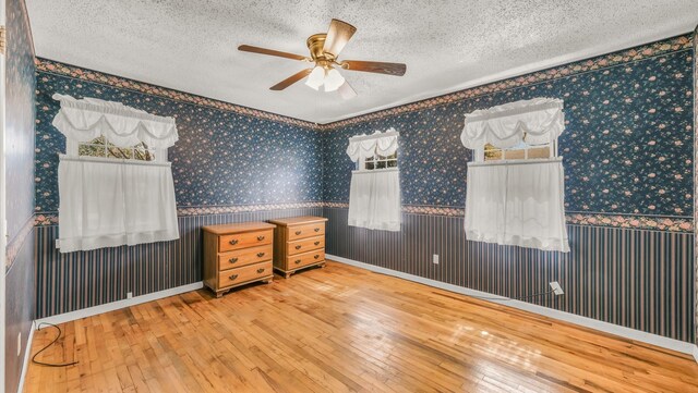 bedroom with a textured ceiling, hardwood / wood-style floors, wainscoting, and wallpapered walls