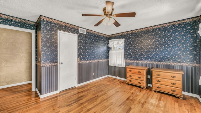 unfurnished bedroom with visible vents, wallpapered walls, a wainscoted wall, a textured ceiling, and wood-type flooring