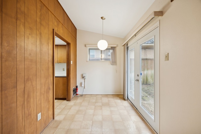 unfurnished dining area featuring lofted ceiling, wooden walls, and light floors