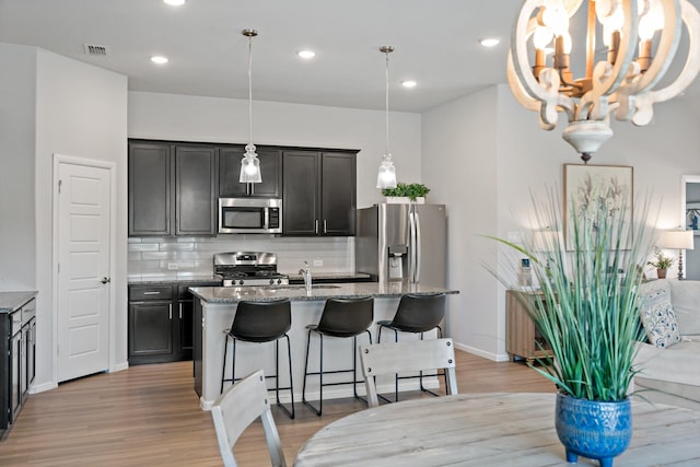 kitchen with a kitchen breakfast bar, appliances with stainless steel finishes, light stone countertops, tasteful backsplash, and an island with sink