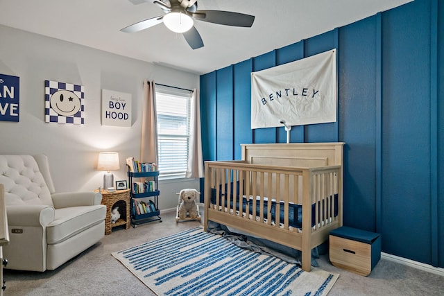 bedroom featuring a crib, carpet, baseboards, and a ceiling fan