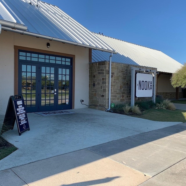 property entrance featuring metal roof, stone siding, french doors, stucco siding, and a standing seam roof