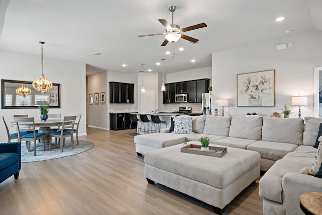 living room with ceiling fan with notable chandelier, light wood-type flooring, baseboards, and recessed lighting