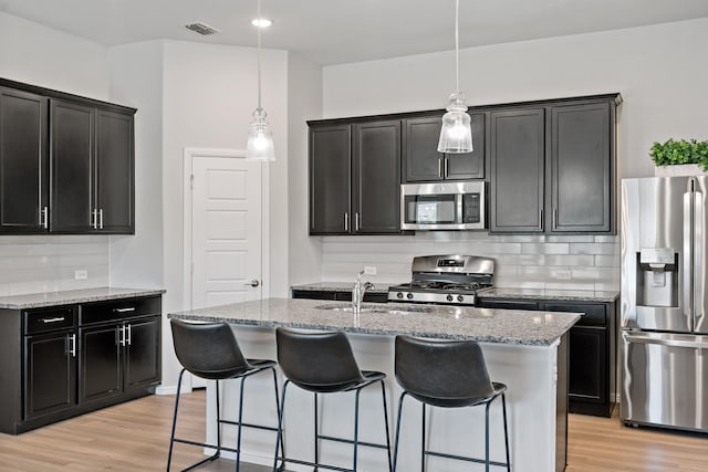 kitchen with light wood-style flooring, visible vents, appliances with stainless steel finishes, dark cabinetry, and backsplash