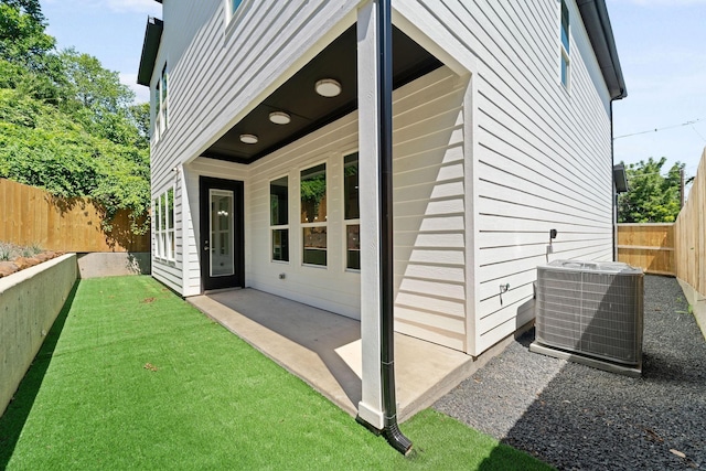 entrance to property with cooling unit, a patio area, fence, and a lawn