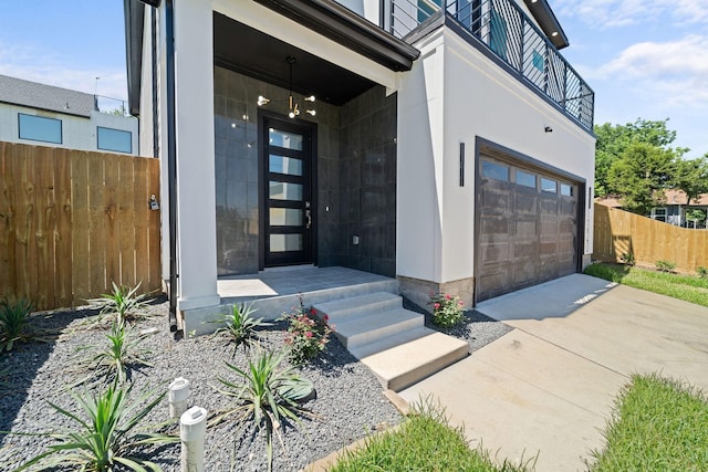 view of exterior entry featuring a garage, fence, driveway, and a balcony