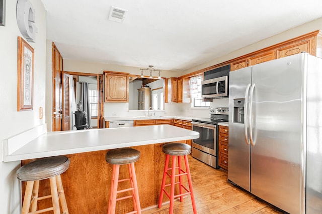 kitchen with stainless steel appliances, a peninsula, a sink, visible vents, and light wood-style floors