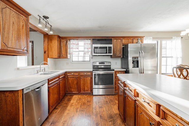 kitchen with appliances with stainless steel finishes, brown cabinets, dark wood-style flooring, light countertops, and a sink