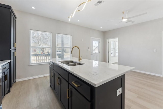 kitchen with light wood-type flooring, baseboards, a sink, and a center island with sink