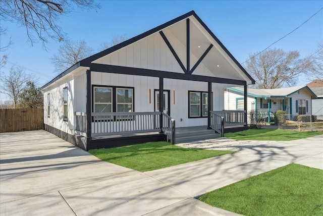 view of front facade featuring covered porch, fence, concrete driveway, and a front yard