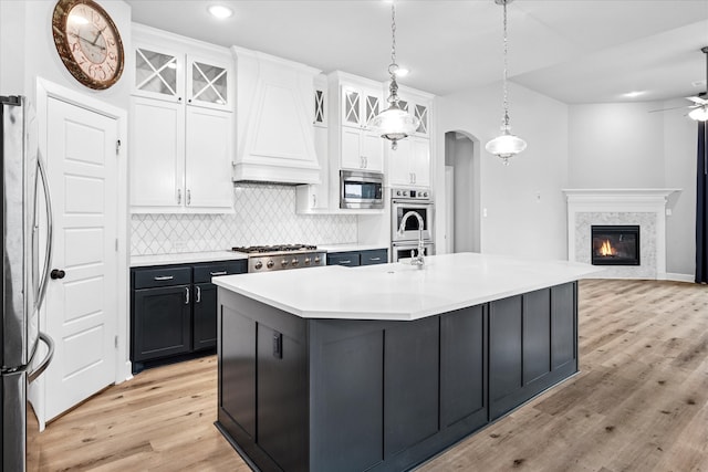 kitchen with arched walkways, white cabinets, stainless steel appliances, premium range hood, and backsplash