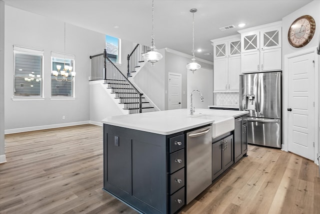 kitchen with stainless steel appliances, light countertops, white cabinetry, a sink, and light wood-type flooring