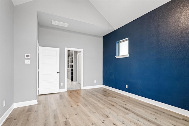 empty room with lofted ceiling, visible vents, an accent wall, wood finished floors, and baseboards