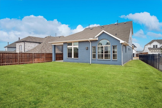 back of house featuring brick siding, a lawn, a shingled roof, and a fenced backyard