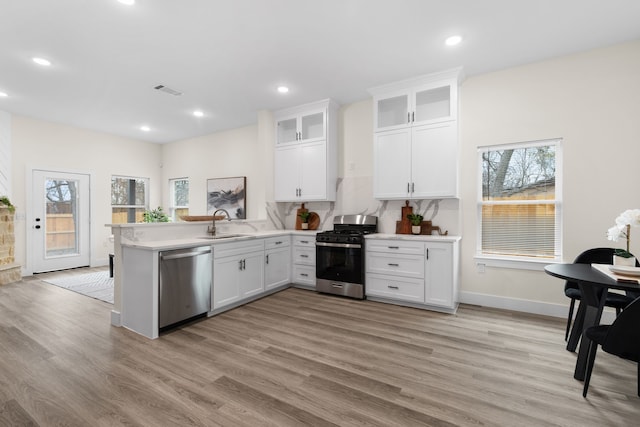 kitchen with appliances with stainless steel finishes, light wood-style floors, white cabinetry, a sink, and a peninsula