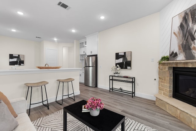 living room featuring light wood finished floors, a fireplace, visible vents, and baseboards